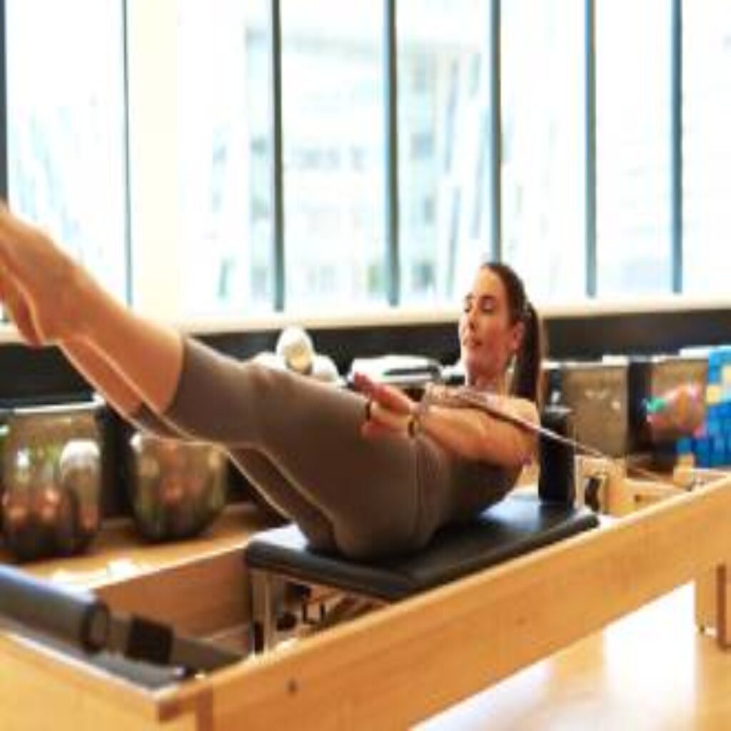 A woman is doing pilates on the reformer.
